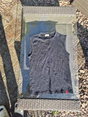 Diesel Svart ärmlös linnetopp - Svart ärmlös linnetopp från diesel med rund halsringning och en liten röd etikett nertill. Enkel och stilren design som passar perfekt till jeans eller shorts. Mjuk och bekväm känsla, perfekt för varma dagar. Sitter som en m-s