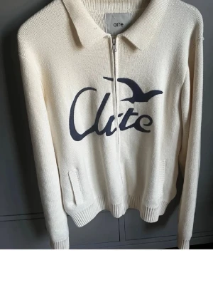 Köp fö fan - Snygg vit stickad ziptröja från Arte med blått tryck och fågelmotiv på bröstet. Tröjan har krage, dragkedja framtill och två fickor. Perfekt för dig som gillar stilren design med en twist.