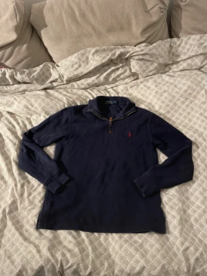  Polo Ralph Lauren quarter zip  - Mörkblå långärmad tröja från Polo Ralph Lauren med halvzip och klassisk krage. Tröjan har det ikoniska röda Polo-logot på bröstet och dragkedja med läderdetalj. Perfekt för en avslappnad men ändå stilren look.