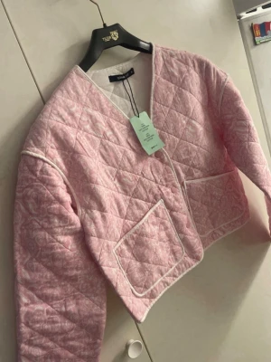 Quiltad rosa cardiganjacka från Gina Tricot - Supersöt quiltad cardiganjacka i ljusrosa från Gina Tricot. Jackan har vita detaljer, två stora fickor fram och ett diskret mönster. Croppad modell med v-ringad hals och knappar framtill. Perfekt för dig som vill ha en trendig och mysig look.