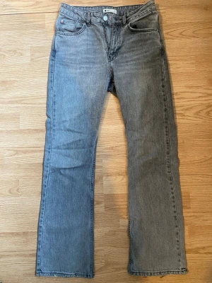 Gråa jeans Gina - Säljer ett par grå jeans med rak/ flared passform och midwaist. Klassisk femficksmodell med knapp och dragkedja framtill. Jeansen är i ett mjukt denimtyg och har en avslappnad look som passar till det mesta. Dom är lite sönder längst ner men inget man lägger mycket märke till.