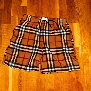 Rutiga shorts med snörning - Snygga shorts med klassiskt brunt, svart, vitt och rött rutmönster. De har elastisk midja med svart snörning för skön passform. Perfekta för sommaren och har en avslappnad vibe. Passar dig som gillar streetstyle och vill sticka ut lite extra.