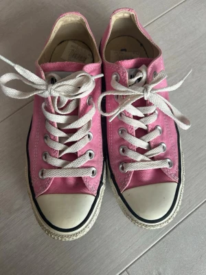 Rosa Converse All Star låga sneakers - Säljer ett par klassiska Converse All Star sneakers i rosa canvas med vita gummisulor och tåhätta. Skorna har vita snören och svarta detaljer längs sulan. Perfekta för dig som vill ha en färgglad och tidlös stil.