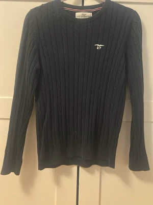 Mörkblå kabelstickad tröja  - Mörkblå kabelstickad tröja från Hampton Republic med rund halsringning och broderad logga på bröstet. Tröjan har långa ärmar och ribbade muddar. Perfekt för lager-på-lager och klassisk stil. Tröjan har ett litet hål vid handleden som knappt syns och som enkelt går att sy igen. Säljer då den ej kommer till användning 💕 storlek 146/152 men skulle säga att den passar en xs/s. Pris kan diskuteras!