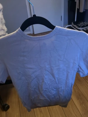 Vit kortärmad topp i bomull - En basic vit topp med korta ärmar och rund halsringning. Tillverkad i mjuk bomull, perfekt för en enkel och clean look. Passar till det mesta och är lätt att matcha med andra plagg.