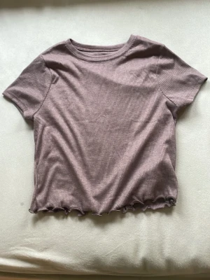 Ljusbrun ribbad croppad topp - Säljer en ljusbrun ribbad croppad topp med korta ärmar och vågig kant nertill. Toppen har en enkel och stilren design som passar perfekt till jeans eller kjol. Superfin färg och mjukt material.