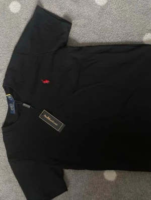Svart t-shirt från Polo Ralph Lauren - Svart t-shirt från Polo Ralph Lauren med klassisk passform och korta ärmar. T-shirten har en liten röd broderad logga på bröstet och är gjord i mjuk bomull. Perfekt för en stilren och enkel look.