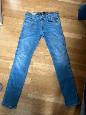 Blå slim fit jeans från Replay - Snygga blå slim fit jeans från Replay, modell Anbass. Klassisk femficksdesign med dragkedja och knapp framtill. Jeansen har en fräsch tvätt och smal passform som sitter tajt längs benen. Perfekta för en trendig och avslappnad look.