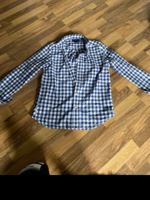 Blårutig skjorta i bomull - Klassisk blårutig skjorta med lång ärm och knappar framtill. Skjortan har en avslappnad passform och är tillverkad i mjuk bomull, perfekt för en stilren vardagslook. Märket är Ralph lauren