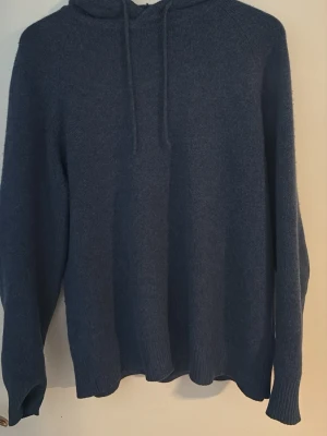 Soft goat-Kashmir hoddie - En enkel och stilren mörkblå hoodie med huva och dragsko. Tillverkad i ett mjukt, stickat material som känns skönt mot huden. Hoodien har långa ärmar och ribbade muddar vid ärmslut och nederkant. Perfekt för en avslappnad look. Ny pris-3899 mitt pris 1050kr