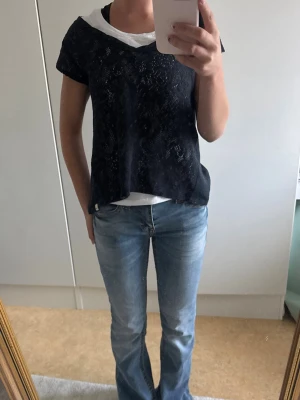 Blå stickad spets topp med v-ringning - Mörkblå stickad topp i spetsmaterial med v-ringning och korta ärmar. Toppen är något transparent och har en lös passform, perfekt att styla över ett linne eller t-shirt. Enkel och stilren design som passar till jeans eller kjol.