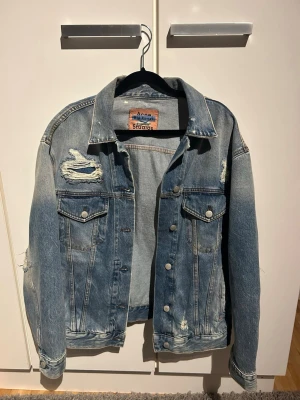 Acne Studios Blå Konst jeansjacka - Säljer en snygg blå jeansjacka från Acne Studios Blå Konst med slitna detaljer och klassisk passform. Jackan har två bröstfickor med lock och knappar framtill. Perfekt för dig som gillar en trendig och avslappnad stil. Oversized men passar mig xs-s🫶