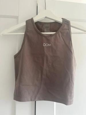Brun/lila crop top från DOM - Snygg brun/lila crop top från DOM med rund halsringning och ärmlös design. Tillverkad i ett stretchigt och mjukt material som passar perfekt till träning eller sportiga outfits. Diskret logga framtill i vitt.