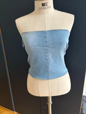 Ljusblå denim tubtopp - Blå tubtopp i denim med bandeau-modell. Toppenhar öppna sidor med tre smala band som håller ihop plagget, omsydd hemma.