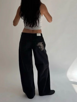 Svarta wide leg-jeans med leopardtryck - Coola svarta jeans från "In Print we Trust" med wide leg-passform och ett stort leopardtryck på bakfickan. Jeansen har låg midja, raka ben och klassiska fickor. Perfekta för dig som vill sticka ut med en unik detalj. Materialet är denim i bomull. De är helt nya med lappar på. Tyvärr försmå för mig därav jag säljer. Nypris är 922kr + frakt 😊