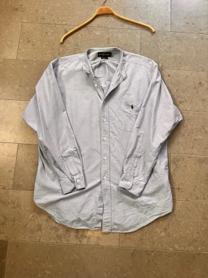 Ljusblå skjorta från Ralph Lauren - Klassisk ljusblå skjorta från Ralph Lauren med knappar hela vägen och broderad logga på bröstet. Skjortan har lång ärm och normal passform, perfekt till jeans eller chinos.
