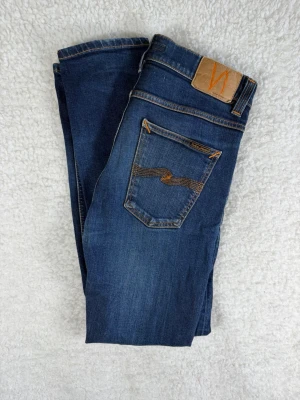 Nudie Jeans Lean Dean (Dry 16 Dips) W32 L32 - Snygga mörkblå  jeans från Nudie med klassiska orange sömmar och vågig detalj på bakfickan. Jeansen har fem fickor och en bekväm passform med stretch. Perfekta för en trendig och avslappnad stil.