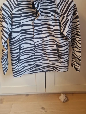 Zebramönstrad jacka från 157 Funk - Cool zebramönstrad jacka från 157 Funk i svart och vitt. Jackan har dragkedjor. . Perfekt för dig som vill sticka ut med ett djurmönster och gillar streetstyle. Den har reflex