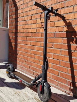 Svart elscooter med LED-belysning - Elektrisk sparkcykel i svart med robust ram och handtag. Utrustad med LED-belysning bak och reflexer på sidorna. Scootern har stora hjul och en bred fotplatta i mörk färg. Perfekt för att ta sig fram snabbt i stan. Materialet är mestadels metall och plast.