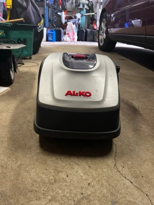 Robotgräsklippare AL-KO Robolinho 500 E - Robotgräsklippare AL-KO Robolinho 500 E i grå och svart plast med röd STOP-knapp på ovansidan. Kompakt och modern design, perfekt för automatiserad gräsklippning. Märket och modellnamnet syns tydligt framtill. Helt nytt batteri bara att installera o köra!