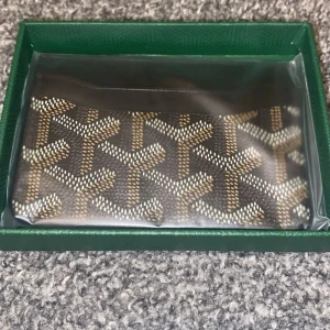  korthållare brun mönstrad - Snygg korthållare i brunt med det klassiska mönstret i beige och vitt. Kommer i en grön ask och är tillverkad i canvasmaterial. Perfekt för att hålla ordning på korten i fickan eller väskan.