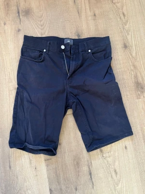 Svarta slim fit shorts från H&M - Säljer ett par svarta slim fit shorts från H&M med klassisk femficksmodell och dragkedja. Shortsen har en stilren look och är tillverkade i ett mjukt bomullsmaterial med lite stretch för extra komfort.
