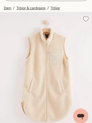 Beige teddyväst med dragkedja - Mysig beige teddyväst från Lindex med hög krage, hel dragkedja framtill och två fickor. Västen har en quiltad bröstficka med dragkedja och är tillverkad i mjukt teddy-material. Perfekt för lager-på-lager och en chill look.
