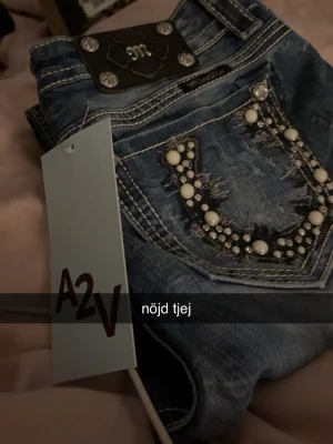 True Religion blå jeans med pärlor - Snygga blå jeans från Miss Me med slitningar och dekorativa pärlor och stenar på bakfickorna. Klassisk femficksmodell med kontrastsömmar och metallknappar. Perfekt för dig som vill sticka ut med detaljer och cool design. Defekter finns på sista sidan. Kontakta för mer information❣️❣️❣️