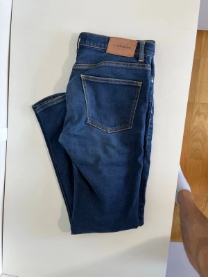 Blå jeans från J.Lindeberg - Snygga blå jeans från J.Lindeberg med klassisk femficksdesign och gul kontrastsöm. En bältenas är sönder (se bild 5). Hör gärna av dig vid frågor!