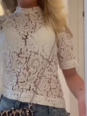 Vit spetsblus med halvärm - Superfin vit blus i spets med blommigt mönster och hög hals. Halvlånga ärmar och genombrutet tyg ger en trendig och romantisk look. Perfekt att styla med jeans eller kjol för en cool vibe.
