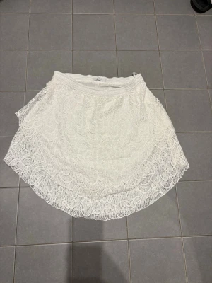 Vit spetskjol från Vila - Supersöt vit kortkjol från Vila med vacker spets och vågig kant. Kjolen har elastisk midja och ett romantiskt uttryck som passar perfekt till sommaren. Lätt att matcha med både toppar och sneakers för en fräsch look.