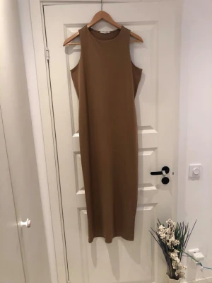 Beige ärmlös långklänning - Säljer en stilren beige långklänning med rund halsringning och ärmlös design. Klänningen har en rak passform och är tillverkad i ett mjukt, stretchigt material som ger en bekväm känsla. Perfekt för dig som gillar minimalistisk och enkel stil.