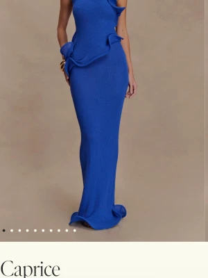 Blå långklänning från Caprice - Elegant blå långklänning från Caprice med asymmetrisk oneshoulder-design och dekorativa volangdetaljer. Klänningen har en figurnära passform och är tillverkad i ett mjukt material som ger en lyxig känsla.