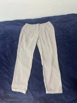 Beige raka linnebyxor - Snygga beige linnebyxor med rak passform och diskreta fickor i sidorna. Byxorna har en enkel design och är tillverkade i ett lätt och luftigt linnematerial, perfekta för en avslappnad och stilren look.