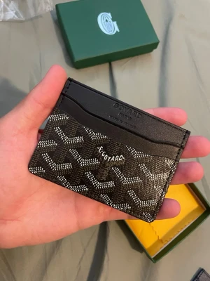 Korthållare  - Snyggt svart korthållare med det klassiska vita och gråa mönstret. Tillverkat i exklusivt läder med flera kortfack och elegant logotyp framtill. Perfekt för dig som vill ha en stilren och lyxig accessoar i fickan.