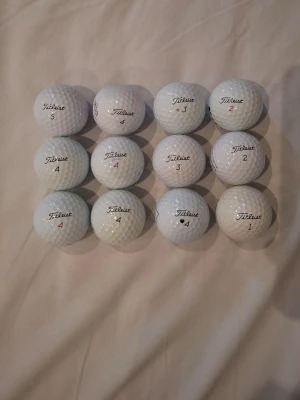 12 vita Titleist golfbollar Pro V1 2 - Säljer 12 stycken vita golfbollar av märket Titleist, modell Pro V1. Bollarna har olika siffror tryckta i rött och svart samt klassisk dimple-yta. Perfekta för dig som vill fylla på golfbagen med kvalitetsbollar.