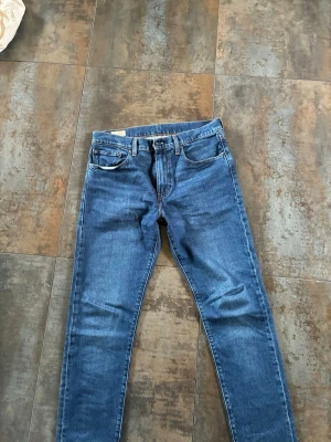 Mörkblå Levi's 512  - Säljer ett par mörkblå Levi's 512 jeans med klassisk femficksdesign och läderpatch bak i midjan. Jeansen är tillverkade i slitstark denim. Perfekta för dig som gillar en tidlös och clean look.