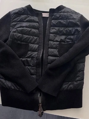 Svart cardiganjacka från Moncler - Säljer min Moncler-kofta i storlek XS.  Priset är förhandlingsbart.  Ullmodell från 2017 i mycket fint skick utan synliga defekter. Modellen är svår att hitta idag.  Observera att QR-koden inte längre går att skanna eftersom koftan syddes in något i midjan på en officiell Moncler-ateljé. En liten del av QR-koden hamnade i sömmen. Detta påverkar inte äktheten – alla etiketter och detaljer är original