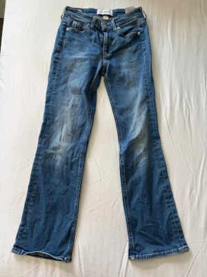Blå bootcut jeans från Calvin Klein - Säljer ett par blå bootcut jeans med snygga slitningar och klassisk femficksdesign. Jeansen har normal midja och är tillverkade i ett mjukt denimtyg. Dressingen är croppad. Passar perfekt till en avslappnad stil och har en tidlös look. Säljer då de inte passar mig längre. Köpare står för frakt