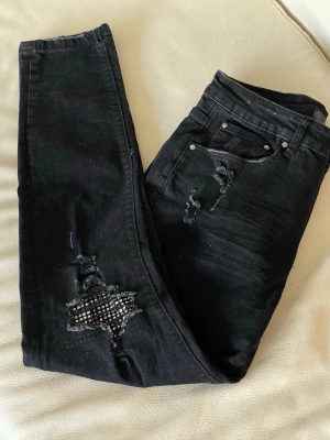 Svarta ripped jeans från Amiri - Säljer ett par svarta jeans från Amiri med slitningar och coola detaljer. Storlek 30 passar S/M 