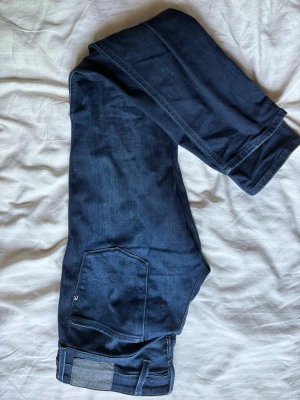 Mörkblå jeans från Replay - Säljer ett par mörkblå jeans från Replay med raka ben och klassisk femficksmodell. Jeansen har en snygg bakficka med Replay-logga och patch i läderimitation vid linningen. Perfekta till en avslappnad och trendig stil.