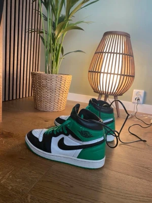 Jordan 1 Mid Grön/Svart/Vit - Säljer ett par Jordan 1 Mid sneakers i grön, svart och vit färg. Skorna har klassisk hög siluett, svart swoosh och gröna detaljer på häl och snörning. Ovandelen är i läder och de har vit mellansula samt grön yttersula. Perfekta för dig som gillar streetwear. De är riktiga och är köpta för över 2000kr för ett tag sen, använd försiktig. Storleken är 44.