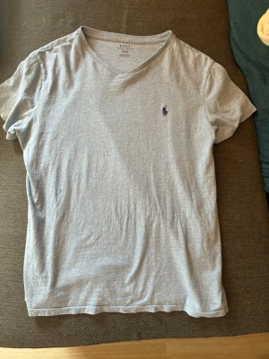 Ljusblå t-shirt från Polo Ralph Lauren - Säljer en mycket fin och knappt använd ljusblå v- ringad t-shirt från polo Ralph Lauren. Är i storlek M men passar som S. På bilderna ser den grå ut men den är ljusblå