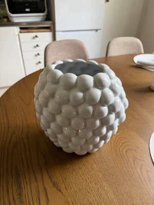 Vit bubblig keramikvas - Säljer en vit vas i keramik med bubblig, rundad struktur som ger ett coolt och modernt intryck. Perfekt som inredningsdetalj på bord eller hylla. Vasen har en blank yta och unik form som sticker ut i rummet.