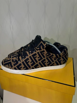 Fendi sneakers med FF-mönster - Har haft dom här skorna ett tag men använder inte dom längre. Dom är i bra skick. Kvitto finns och boxen. Dom är lita konstiga i storleken det står 42EU på kvitto men dom passar mig och jag har storlek 44.