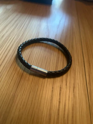 Svart flätat läderarmband - Stilrent svart armband i flätat läder med ett enkelt magnetlås i silverfärgad metall. Perfekt accessoar för dig som gillar minimalistisk och tidlös design. Passar både till jeans och skjorta.