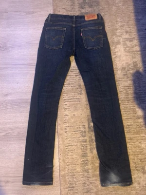 Mörkblå Levi's 512 Slim Jeans - Säljer ett par mörkblå Levi's 512 slim jeans med klassiska bakfickor och gul kontrastsöm. Jeansen har en rak passform och är tillverkade i slitstarkt denim med den ikoniska läderlappen bak i midjan. Perfekta för en avslappnad och stilren look.