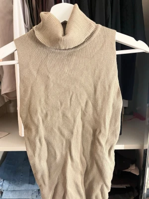 Beige ribbad polotopp ärmlös från Gina tricot - Säljer en beige ärmlös polotopp i ribbad bomullsmix. Toppen har hög polokrage och är figurnära i modellen, perfekt att styla med jeans eller kjol för en clean look.