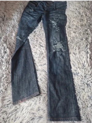 Blå slitna bootcut jeans - Säljer dessa jättefina blå bootcut jeansen med slitningar och trasiga detaljer på låren och knäna. Perfekta för en avslappnad och trendig look. Säljer då jag verkligen behöver plats i garderoben. Midjemåttet är 35 cm, innerbenslängden 80cm och grenmåttet 18cm.