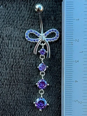 NY oanvänd Navelpiercing med hänge | Kirurgiskt stål | Rosett och lila stenar  - 💕30% Bundle-rabatt vid köp av minst 2 artiklar. ⭐️NY oanvänd piercing i kirurgiskt stål; rostfritt och säkert för läkta piercingar.                               📏MÅTT ⭕️Stavens längd: 10mm ⭕️Stavens tjocklek: 1,6mm ⭕️Smyckets totala längd: 50mm                                                                         🤍Färger: Silver och lila                                                          💌Skickas spårbart via Plick SafePay.